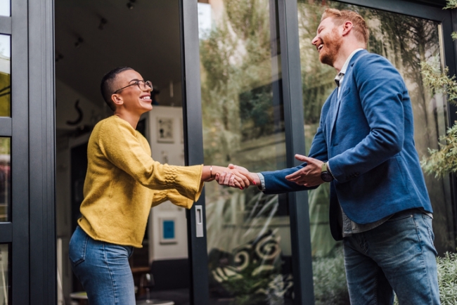A business owner greeting a customer at the door of an office, smiling and shaking hands to build customer retention.