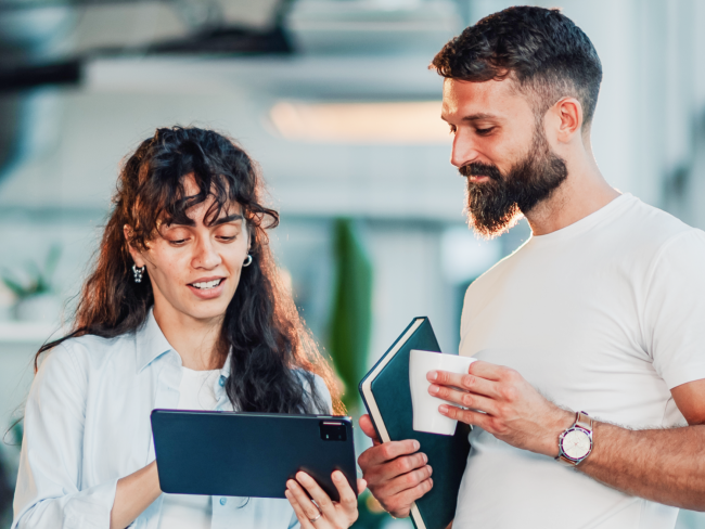A man and a woman in an office look at customer feedback on a tablet